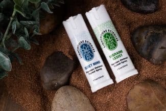 Lighthouse Sciences Migraine Assist & Quiet Mind Precision Metered Topical Sprays laying on sand and rocks